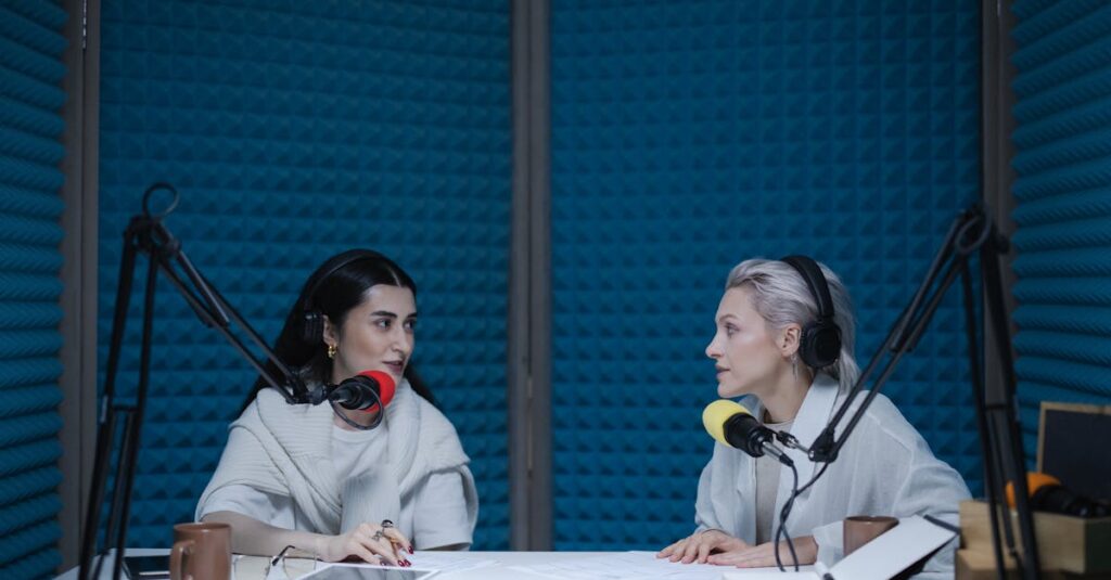 Two women in a soundproof studio recording a podcast with microphones and equipment.